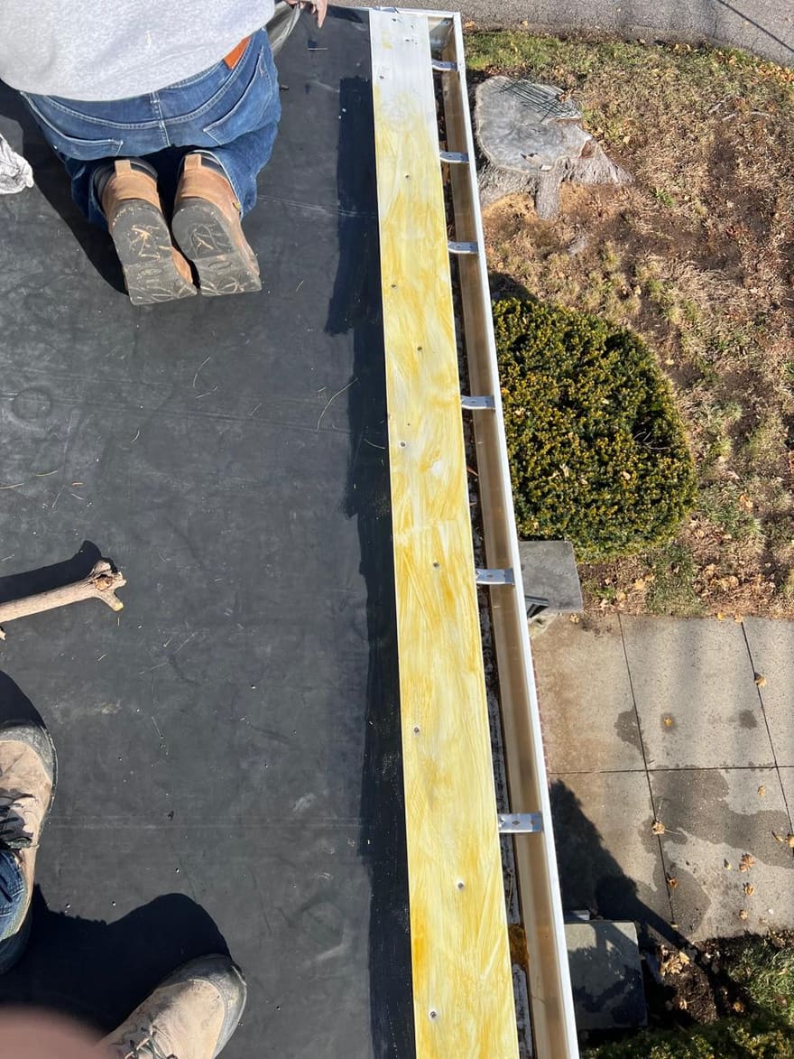 Fresh adhesive rolled along a rubber flat roof at the new gutter line.