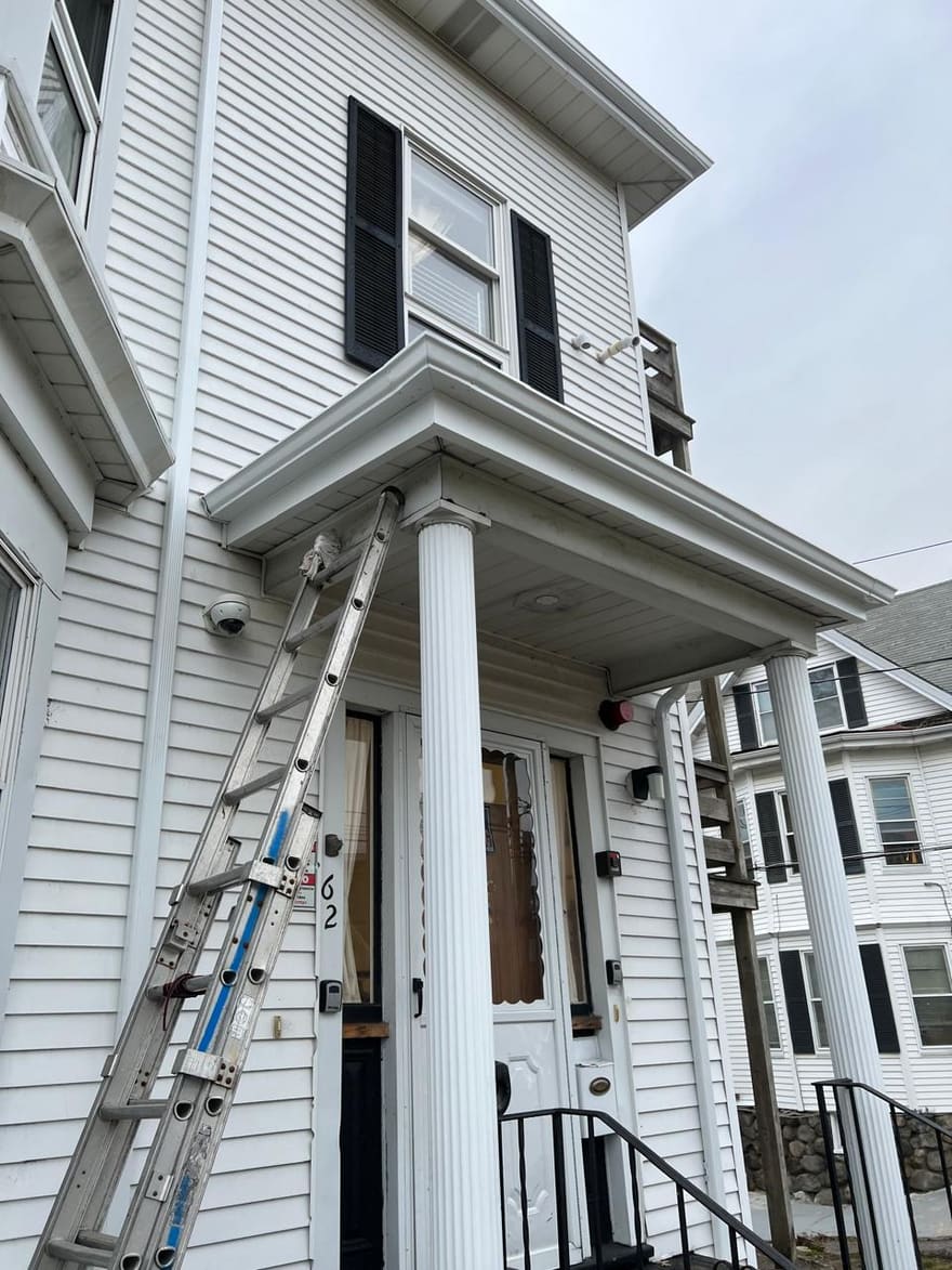 A two-story clapboard house with the crew's ladder set for exterior work.