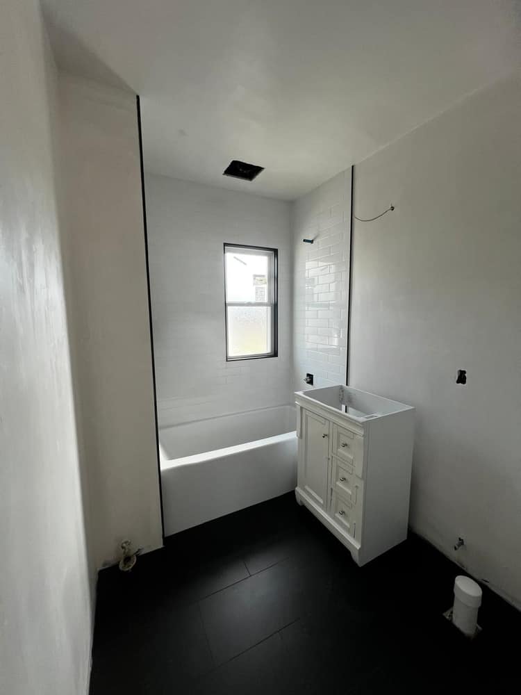 A repainted bathroom in clean white, with a new vanity and a subway-tile surround.