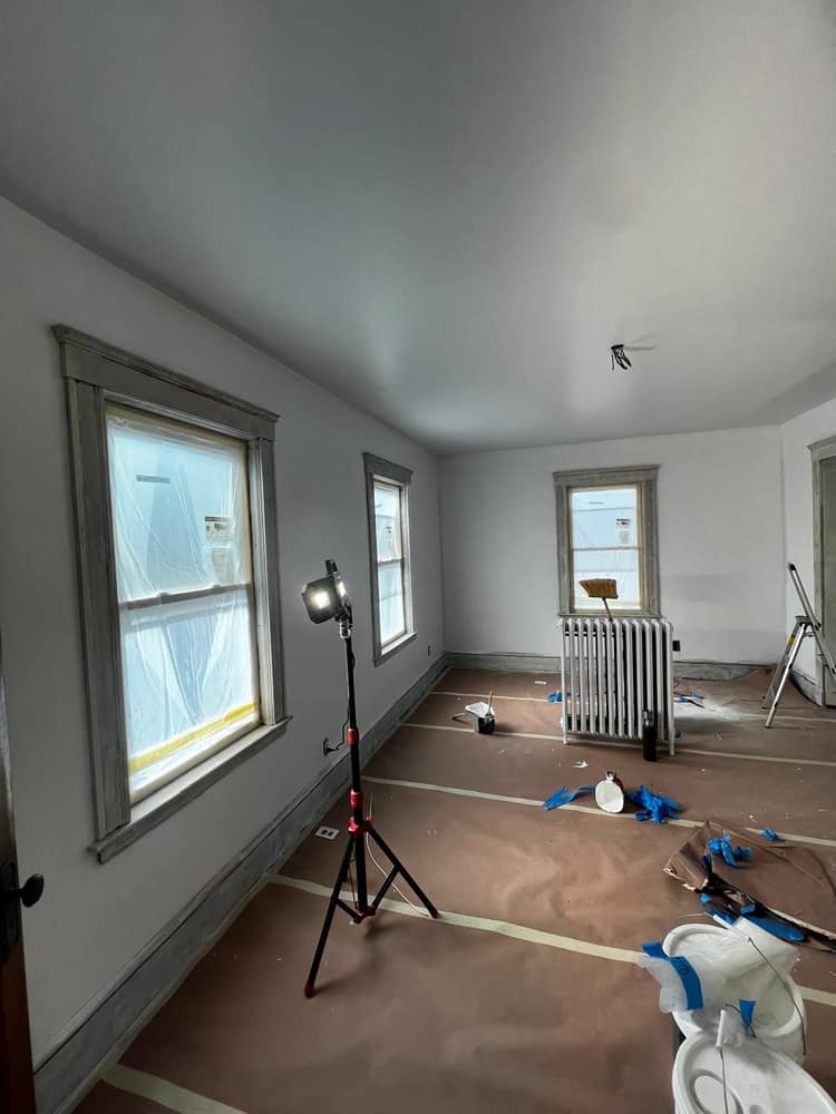 An interior repaint in progress, walls and ceiling coated with the windows masked and the floor papered off.