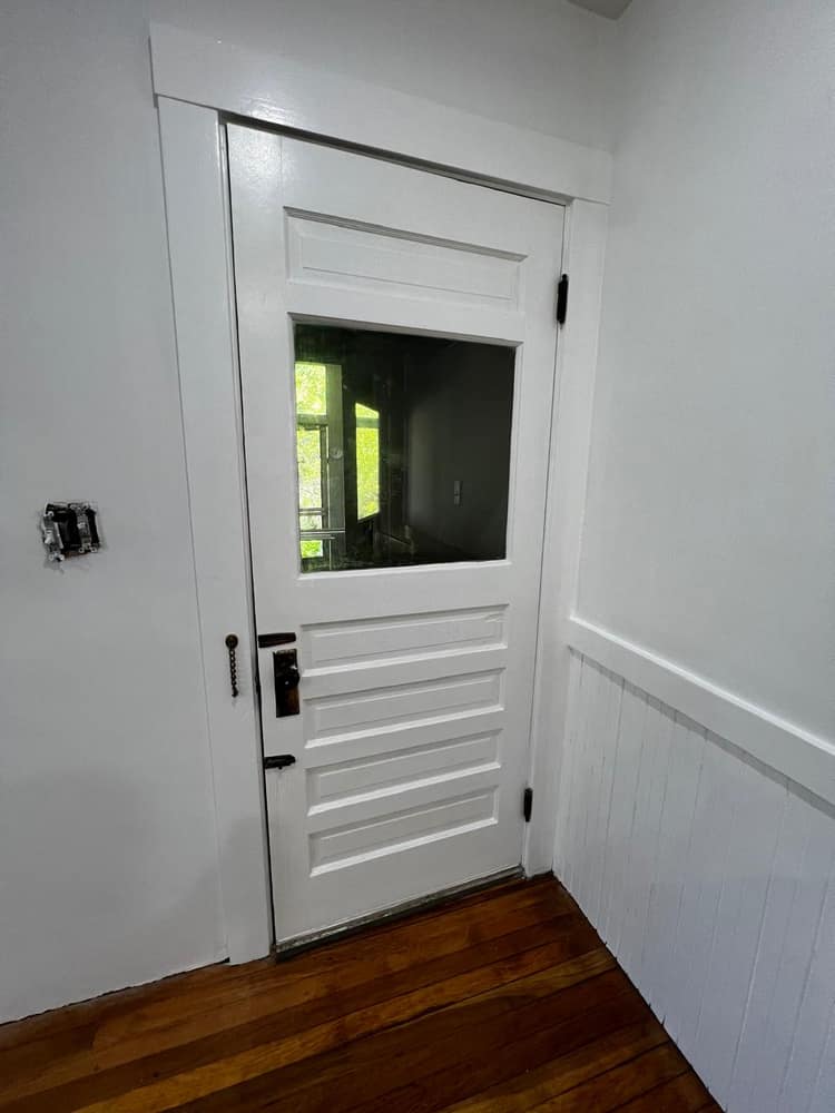 A finished interior door and trim in crisp white over a refinished wood floor.