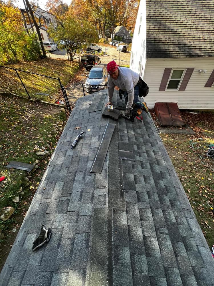Laying new architectural shingles along a low-slope roof section.
