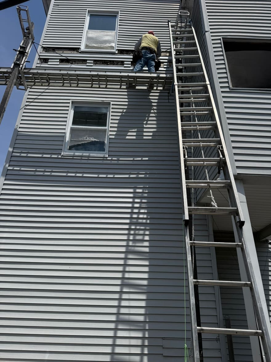 New siding going on over the prepared wall, worked from staging.